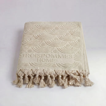 Beige textured throw blanket with tassels on a light gray background